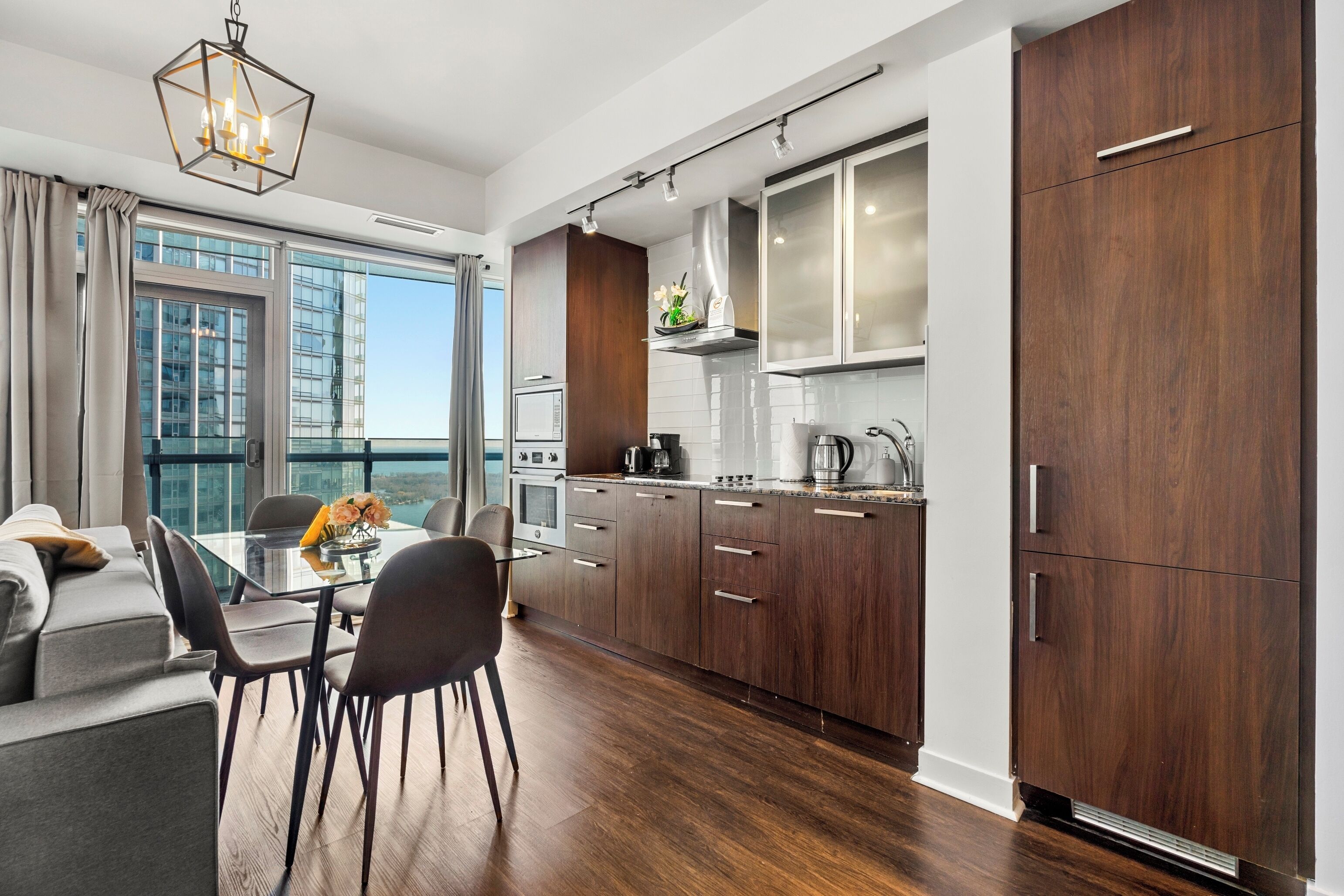 A modern kitchen with dark wood cabinets, stainless steel appliances, and a dining area with a glass table and chairs.