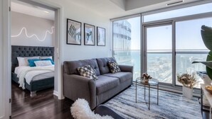 A modern living room with a grey sofa, a bed with a grey headboard, and framed artwork on the wall. - York Suites Toronto (Toronto)