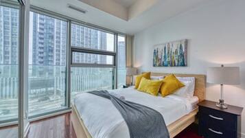 A modern hotel room with a large bed, a nightstand, a lamp, and a painting on the wall.