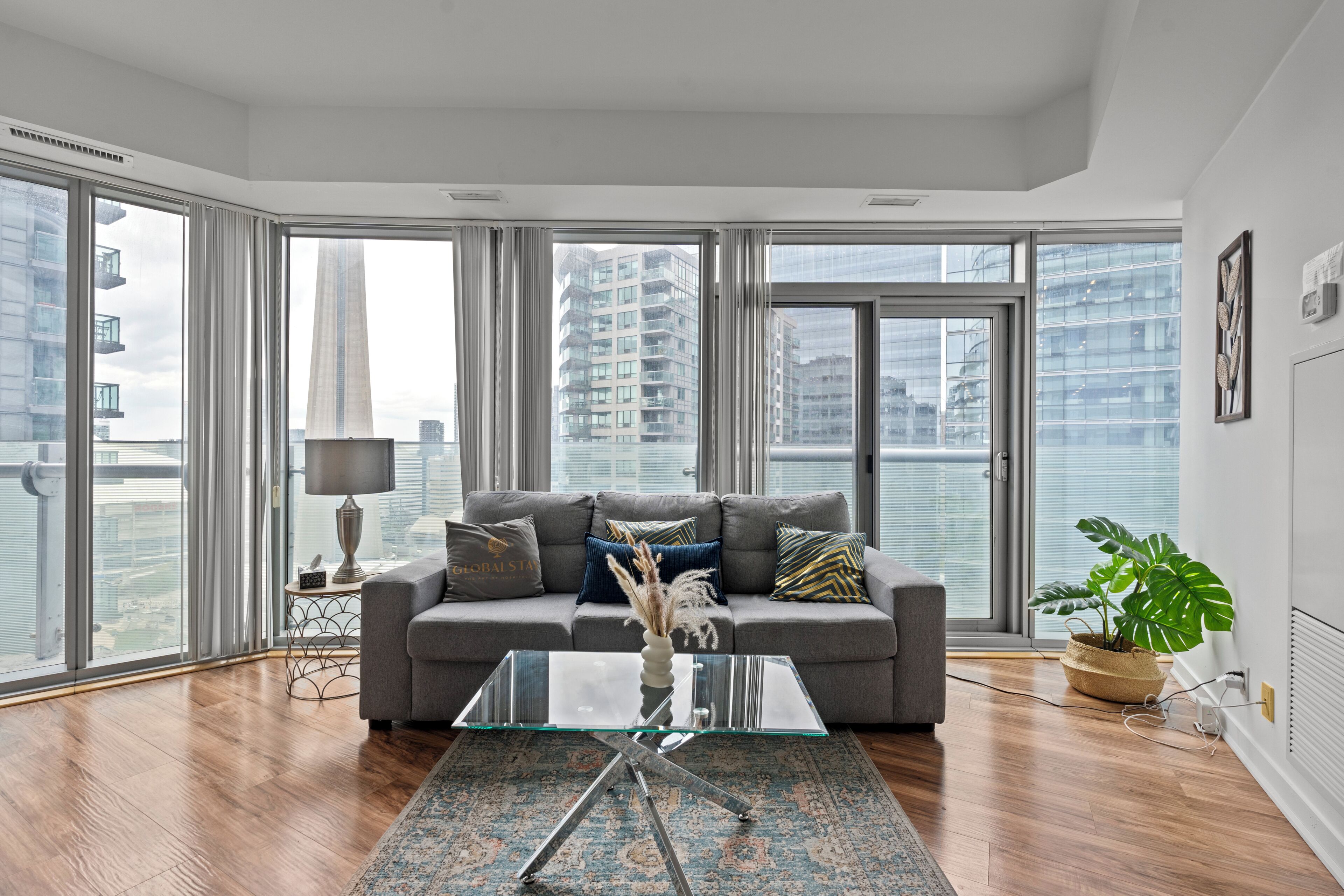 A modern living room with a grey sofa, a glass coffee table, and a large window offering a city view.