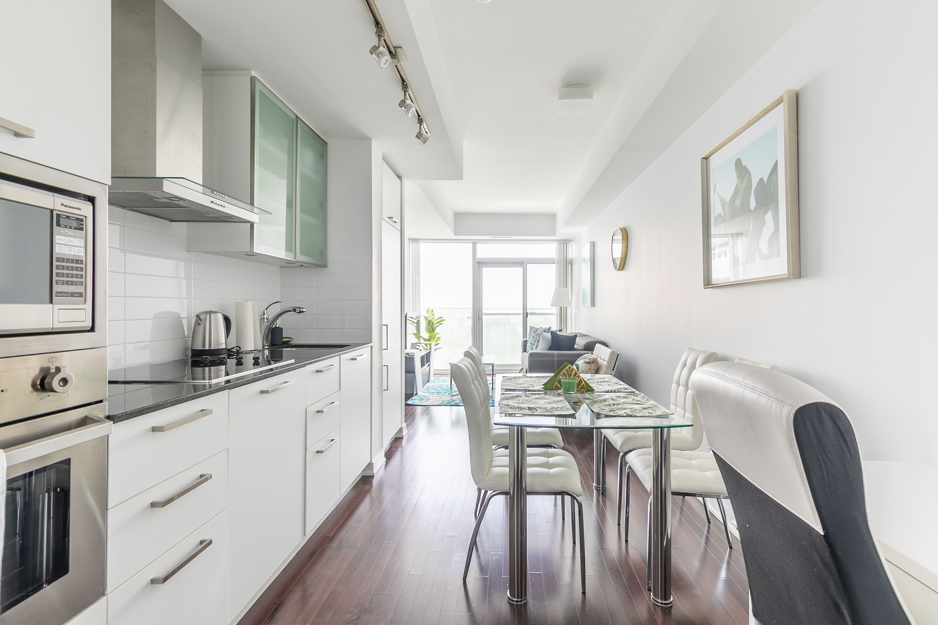 A modern kitchen with white cabinets, stainless steel appliances, and a dining area with a glass table and white chairs.