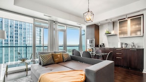 A modern living room with a sofa, a dining table, and a kitchen area with a view of the city. - York Suites Toronto (Toronto)