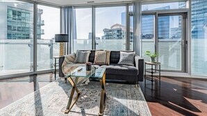 A modern living room with a sofa, glass coffee table, and a view of a cityscape through large windows. - York Suites Toronto (Toronto)