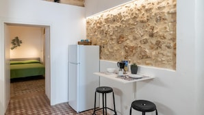 A compact kitchen with a stone wall backsplash, a white refrigerator, and a small bar area with stools. - Dimora Netina by Wonderful Italy (Noto)