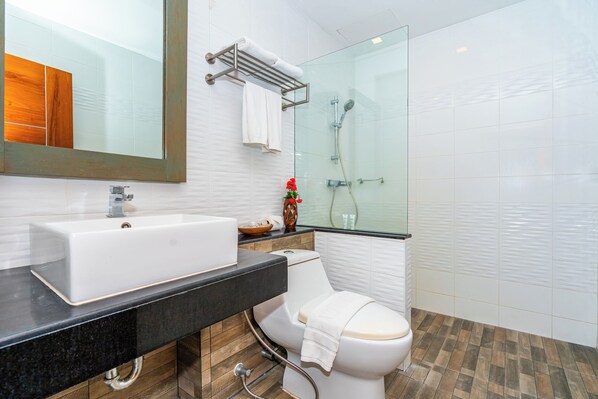 Une salle de bain moderne avec un grand miroir, un lavabo blanc et une douche à parois de verre.