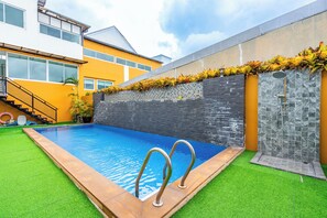 Une piscine avec un mur en pierre et un espace de douche en verre.