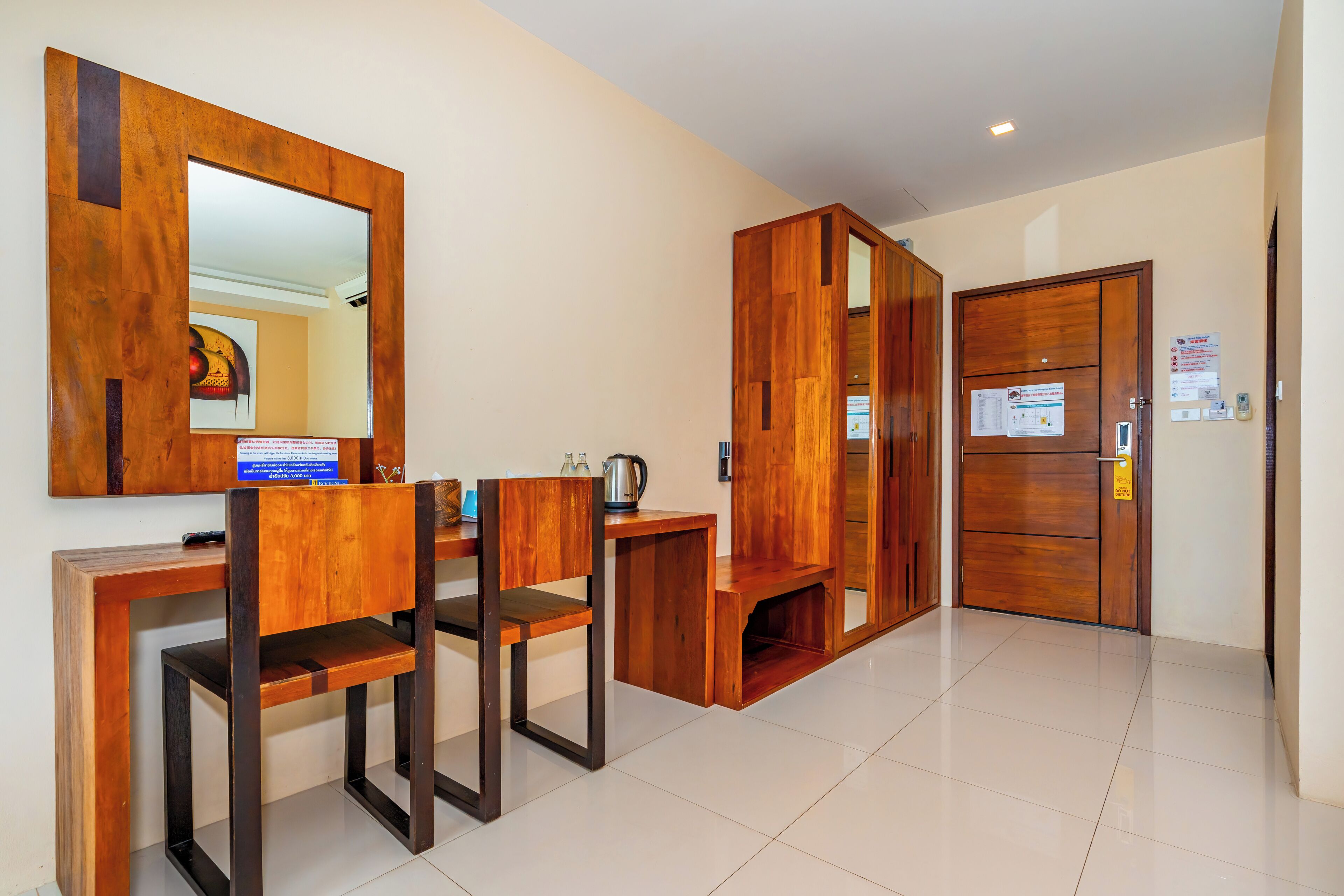 A hotel room with a wooden desk, chairs, a mirror, a door, and a tiled floor.