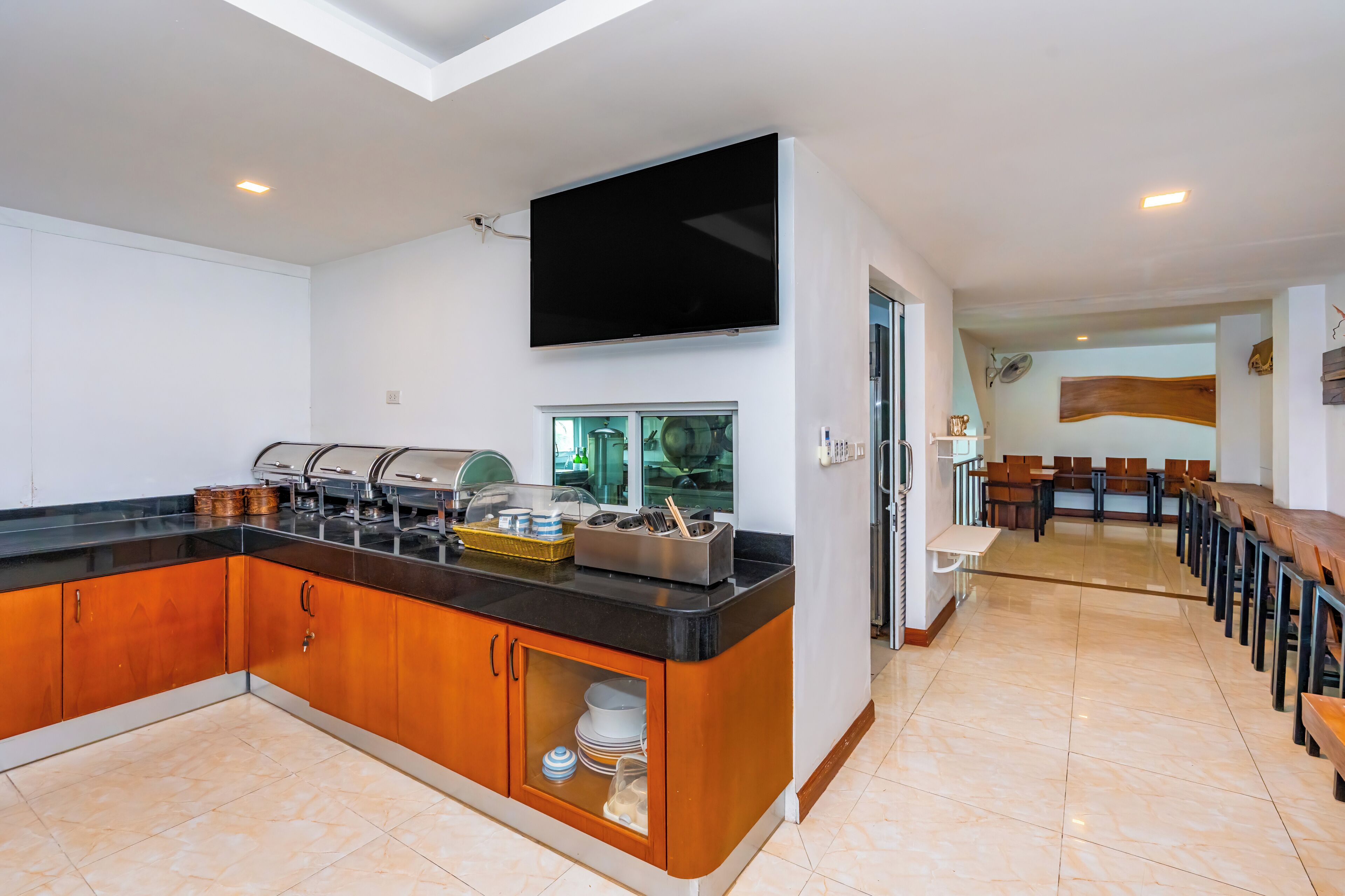 A modern kitchen with a flat-screen TV, buffet setup, and a dining area with wooden tables and chairs.