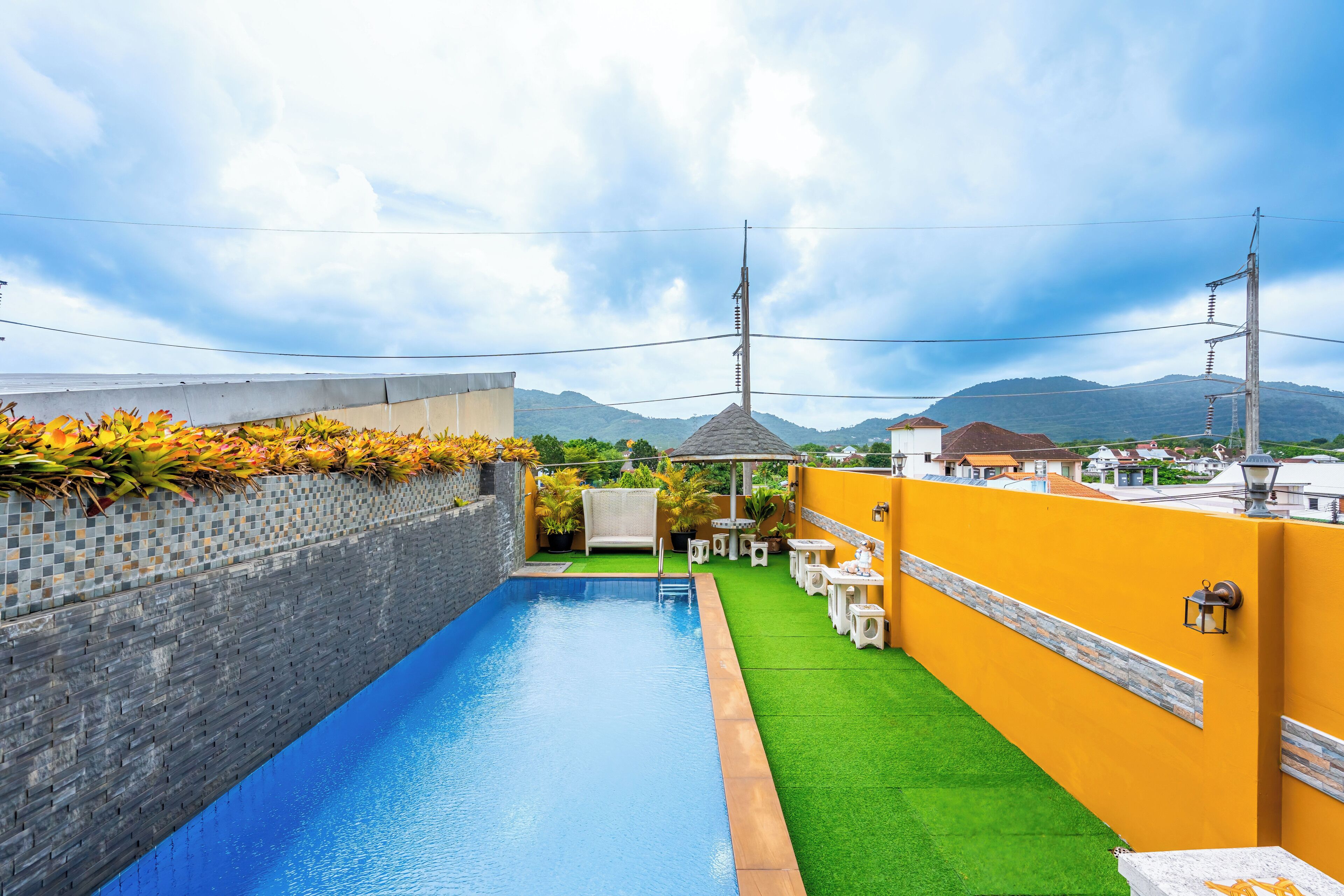A swimming pool with a tiled border, a green artificial lawn, and a yellow wall with a stone accent.