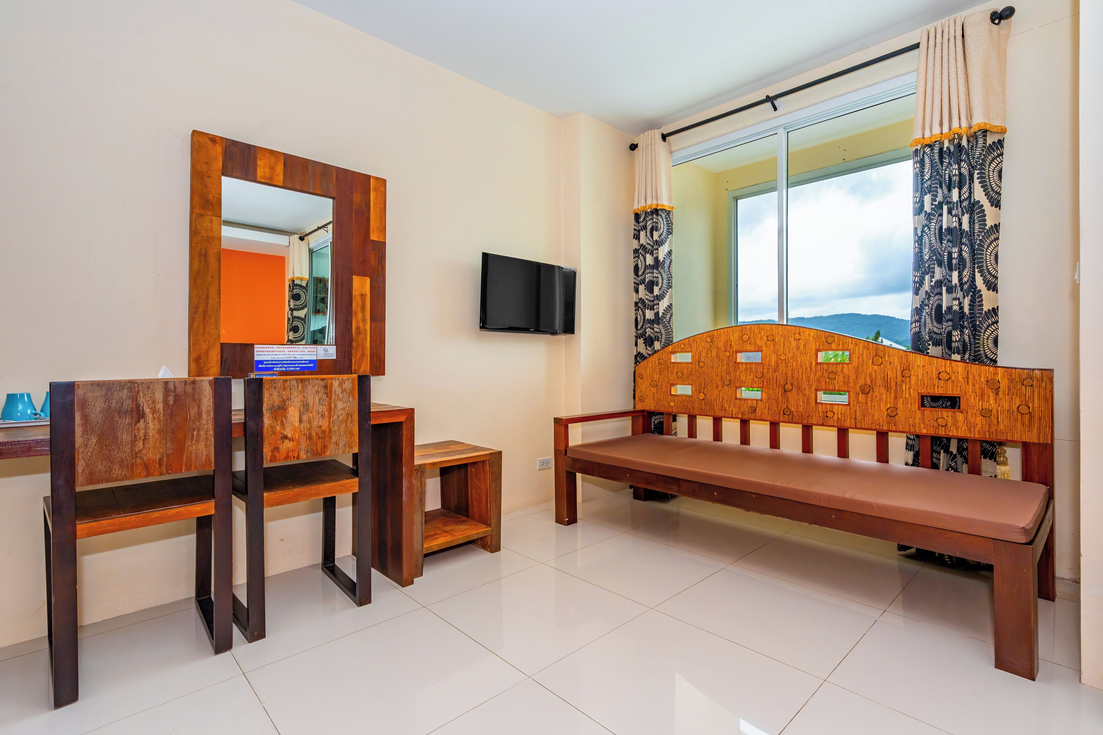 A hotel room with a wooden bench, a small table, a mirror, and a TV mounted on the wall.