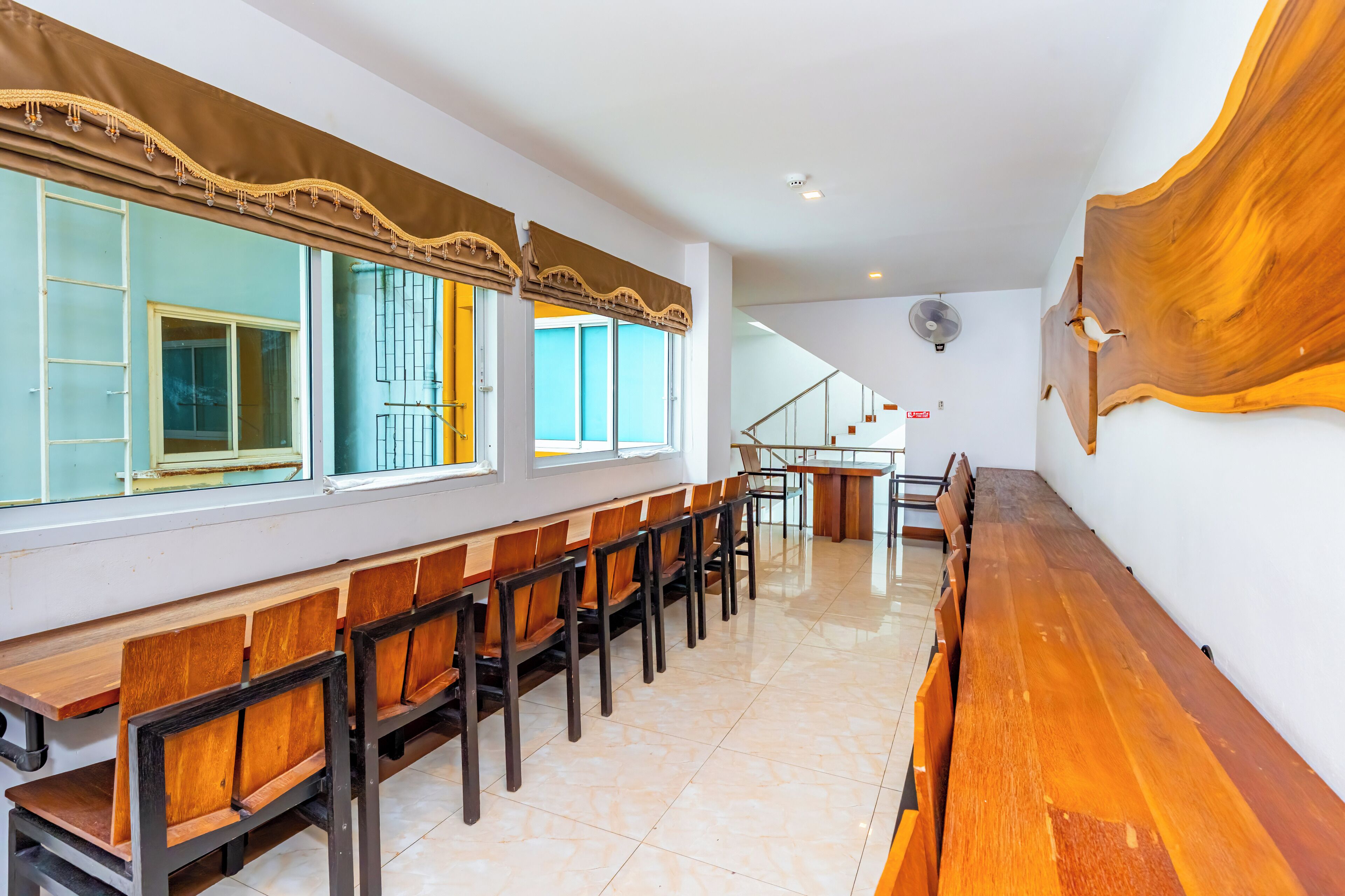 A long wooden bench with chairs along a wall, a staircase, and a large wooden artwork on the wall.