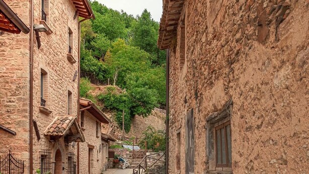 Un estrecho sendero de piedra bordeado por edificios rústicos y un pequeño puente sobre un arroyo.