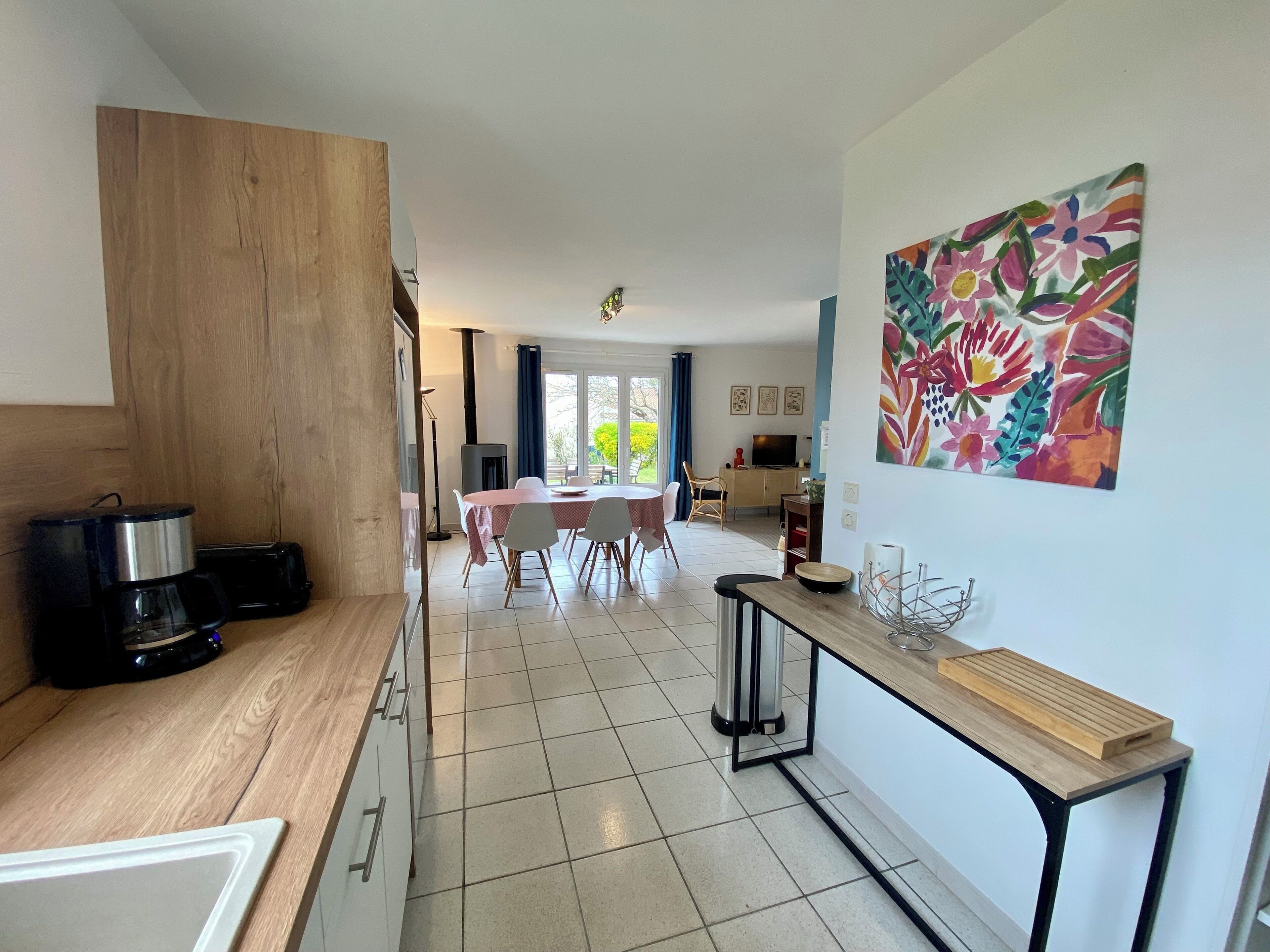 Cozinha moderna com área de refeições, uma janela grande e um quadro floral colorido na parede.