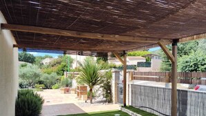 Ein überdachter Patio-Bereich mit einer Holzpergola, einem gepflegten Rasen und Blick auf eine Wohngegend.