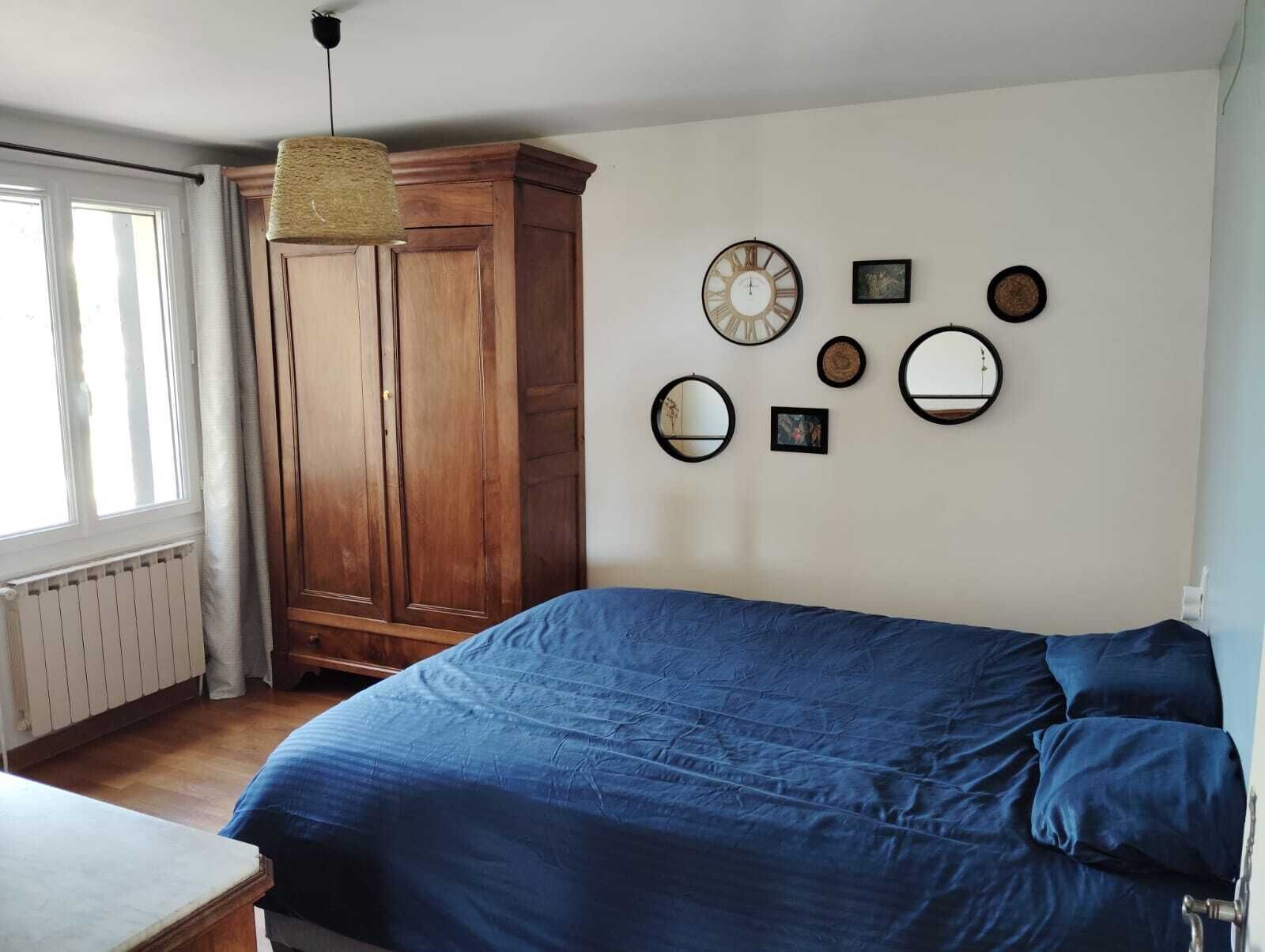 A bedroom with a large bed, a wooden wardrobe, and several wall-mounted mirrors.