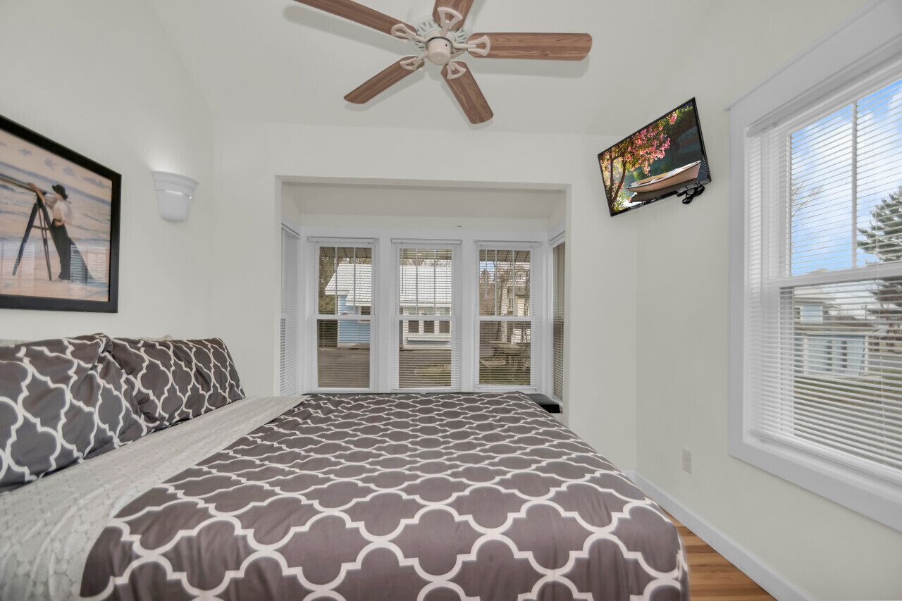 A bedroom with a bed, a ceiling fan, a TV, and a window with blinds.
