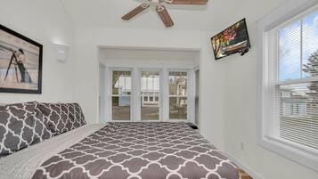 A bedroom with a bed, a ceiling fan, a TV, and a window with blinds.