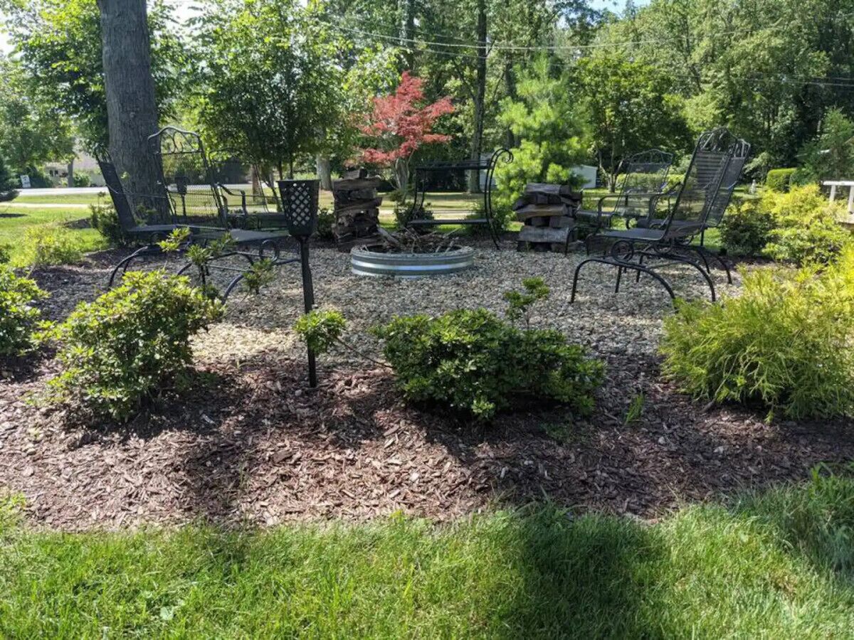 A garden with a circular fire pit, two metal chairs, and various shrubs.