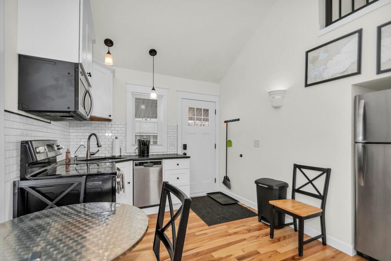 A modern kitchen with white cabinets, stainless steel appliances, a dining table with chairs, and a black trash bin.