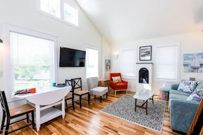 A spacious living area with a dining table, chairs, a red armchair, a sofa, a fireplace, and a television mounted on the wall. - Heron's Nest I Paw Paw Lake Cottages I Huron #1 (Coloma)