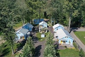 A cluster of blue houses with a central driveway, surrounded by trees. - Heron's Nest I Paw Paw Lake Cottages I Huron #1 (Coloma)