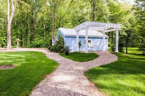 Une maison bleue surmontée d’une pergola blanche, entourée d’un chemin de gravier et d’une végétation luxuriante.