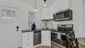 Una cocina moderna con armarios blancos, lavavajillas de acero inoxidable, microondas y horno.