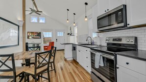 A modern kitchen with white cabinets, a stainless steel microwave, and a wooden dining table with chairs.