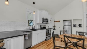 A modern kitchen with white cabinets, a black countertop, and a wooden dining table with chairs.