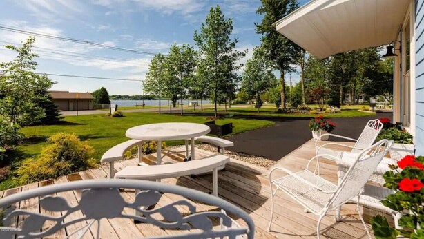 A wooden deck with outdoor furniture, a view of a lake, and a well-maintained lawn.