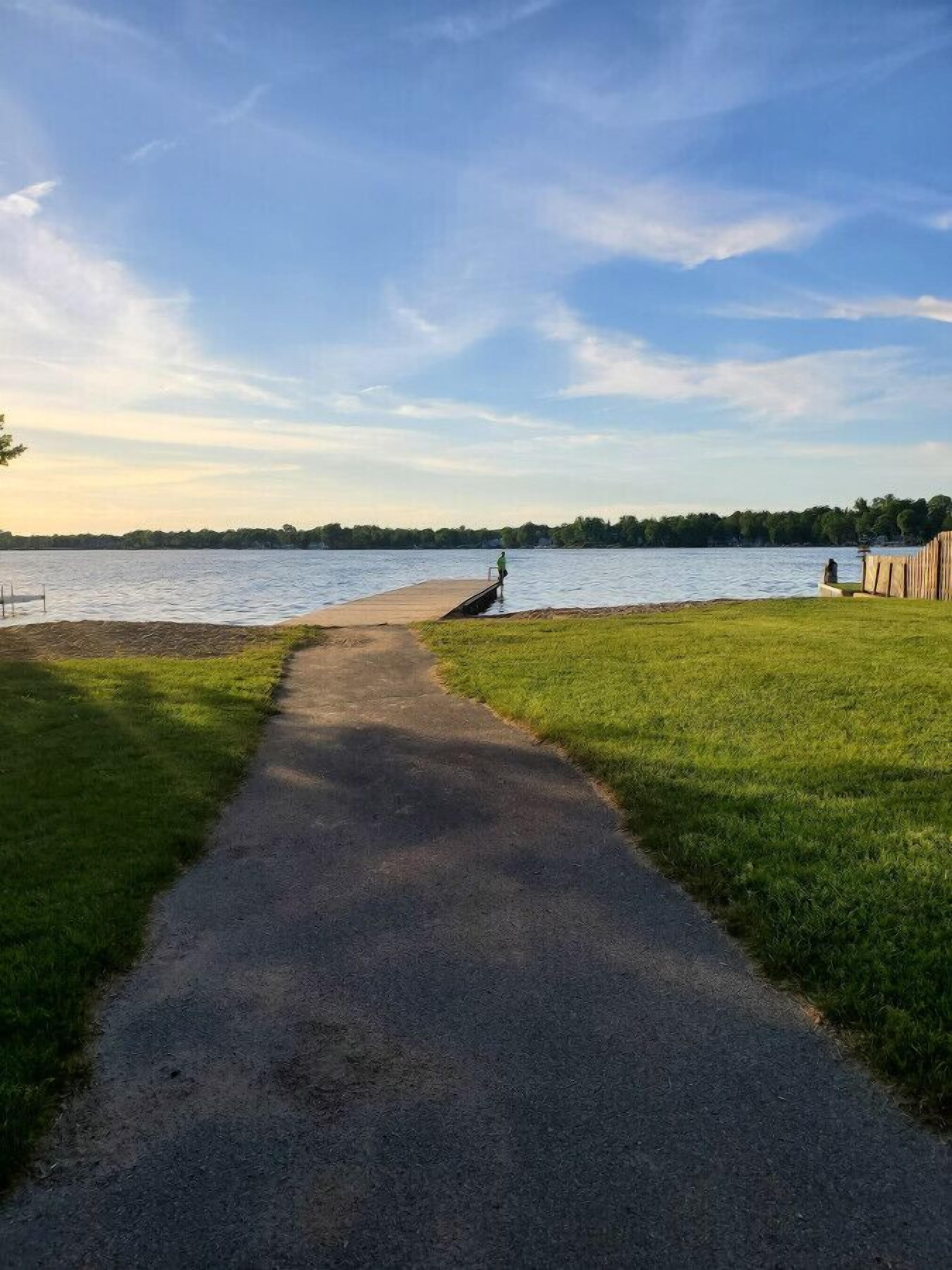 A paved path leading to a lake with a wooden structure on the right.
