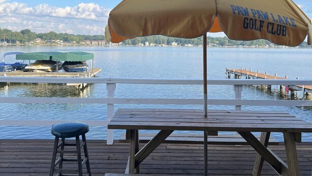 En träveranda med ett picknickbord och ett parasoll med texten ”PAW PAW LAKE GOLF CLUB”.