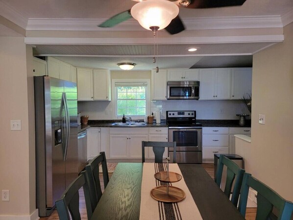 A modern kitchen with white cabinets, stainless steel appliances, and a dining area with a wooden table and chairs. - Little Paw Paw Lake House with Hot Tub (Watervliet)