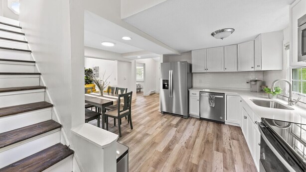 Una cocina moderna con armarios blancos, electrodomésticos de acero inoxidable y piso de madera.
