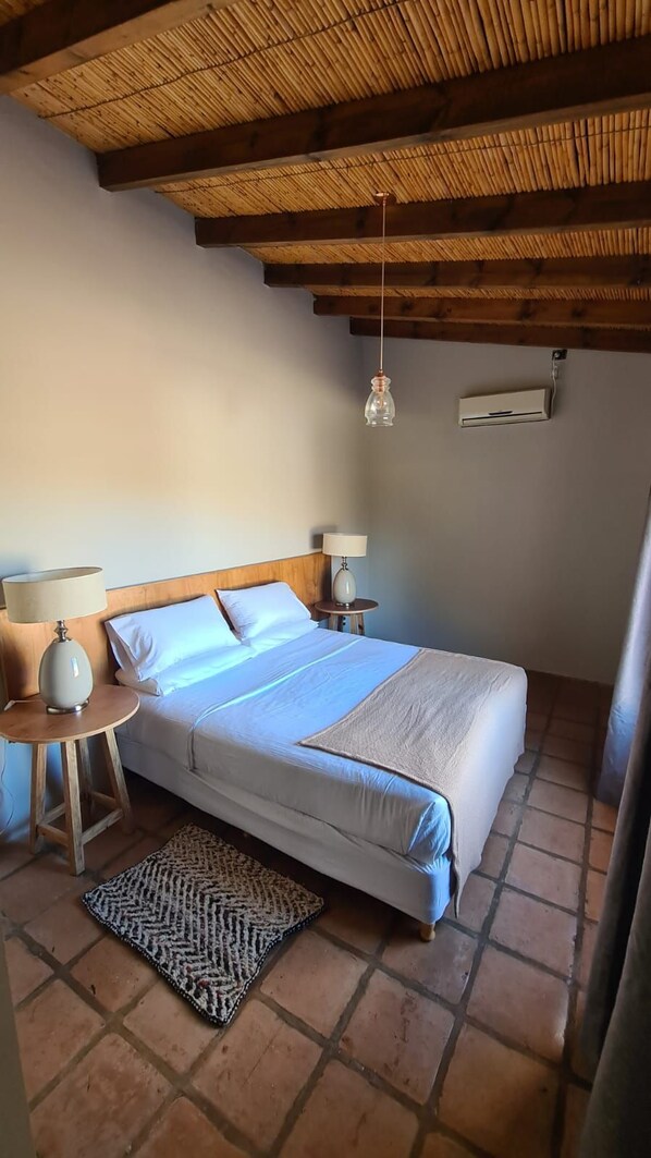 A bedroom with a bed, bedside lamps, a hanging light, and a wall-mounted air conditioner.