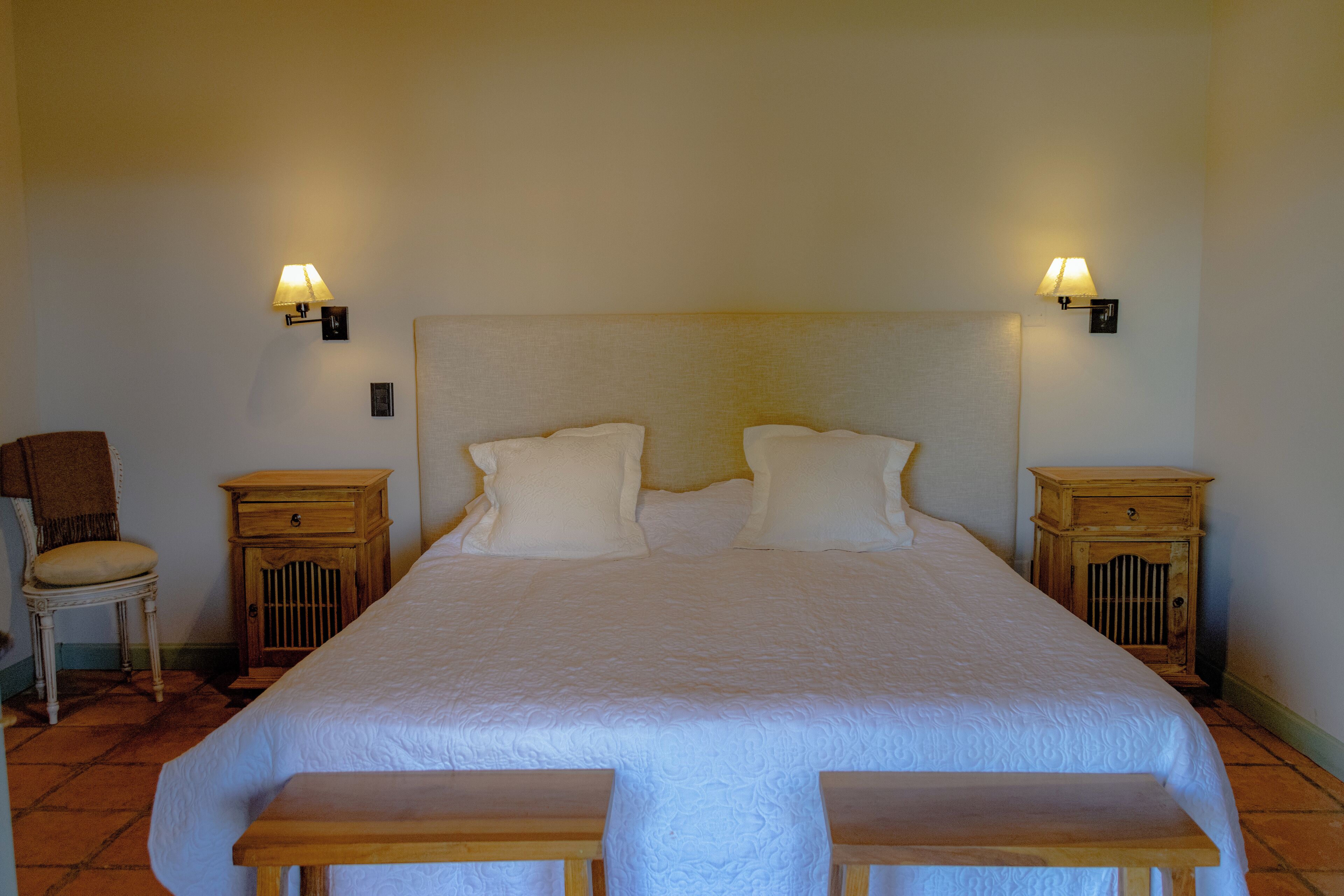 Ein großes Bett mit zwei Nachttischen, einem Sessel und einer Bank in einem Hotelzimmer.