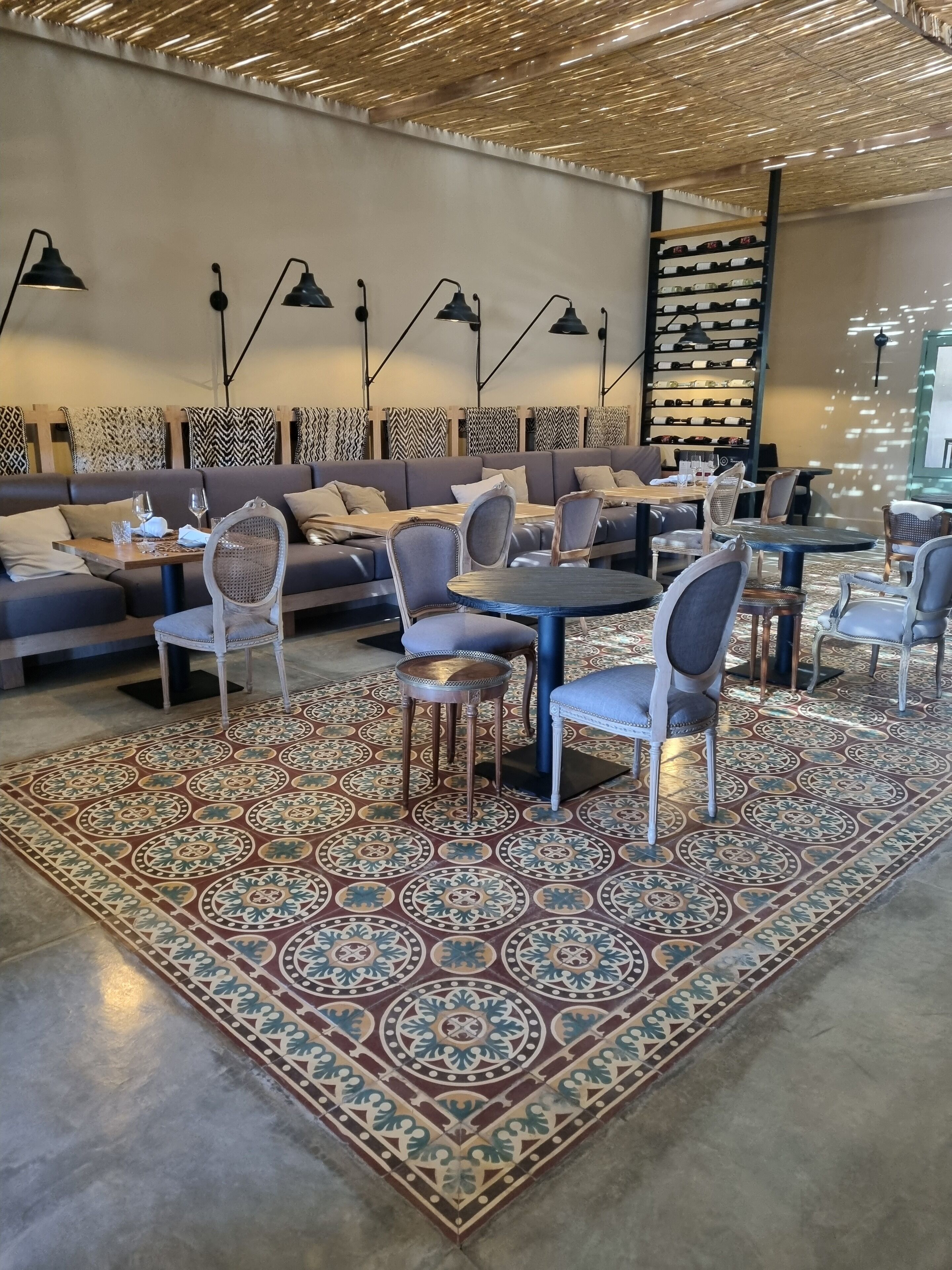 A modern lounge area with sofas, tables, and chairs, a patterned rug, and a wall of wine bottles.