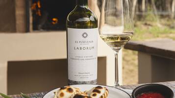 Een fles El Porvenir de Catafalco wijn, een glas witte wijn en een bord met eten op een buitentafel.