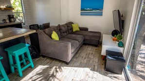 Een moderne woonruimte met een grijze modulaire bank, een smaragdgroen krukje en een flatscreen televisie.