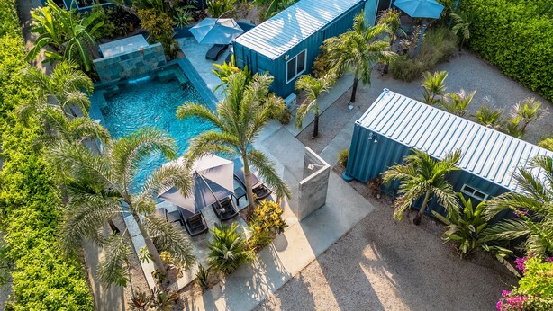 Een modern resort met een zwembad, palmbomen en blauwe gebouwen.