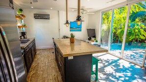 Een moderne keuken met een houten kookeiland, inbouwapparatuur en uitzicht op een tropische tuin door grote schuifdeuren.