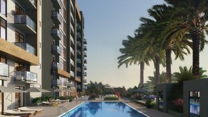 Piscina com espreguiçadeiras e guarda-sóis, cercada por palmeiras e um edifício moderno com varandas.