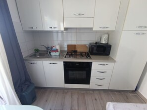 Une cuisine de taille réduite avec des meubles blancs, une cuisinière à gaz, un four à micro-ondes et un évier.