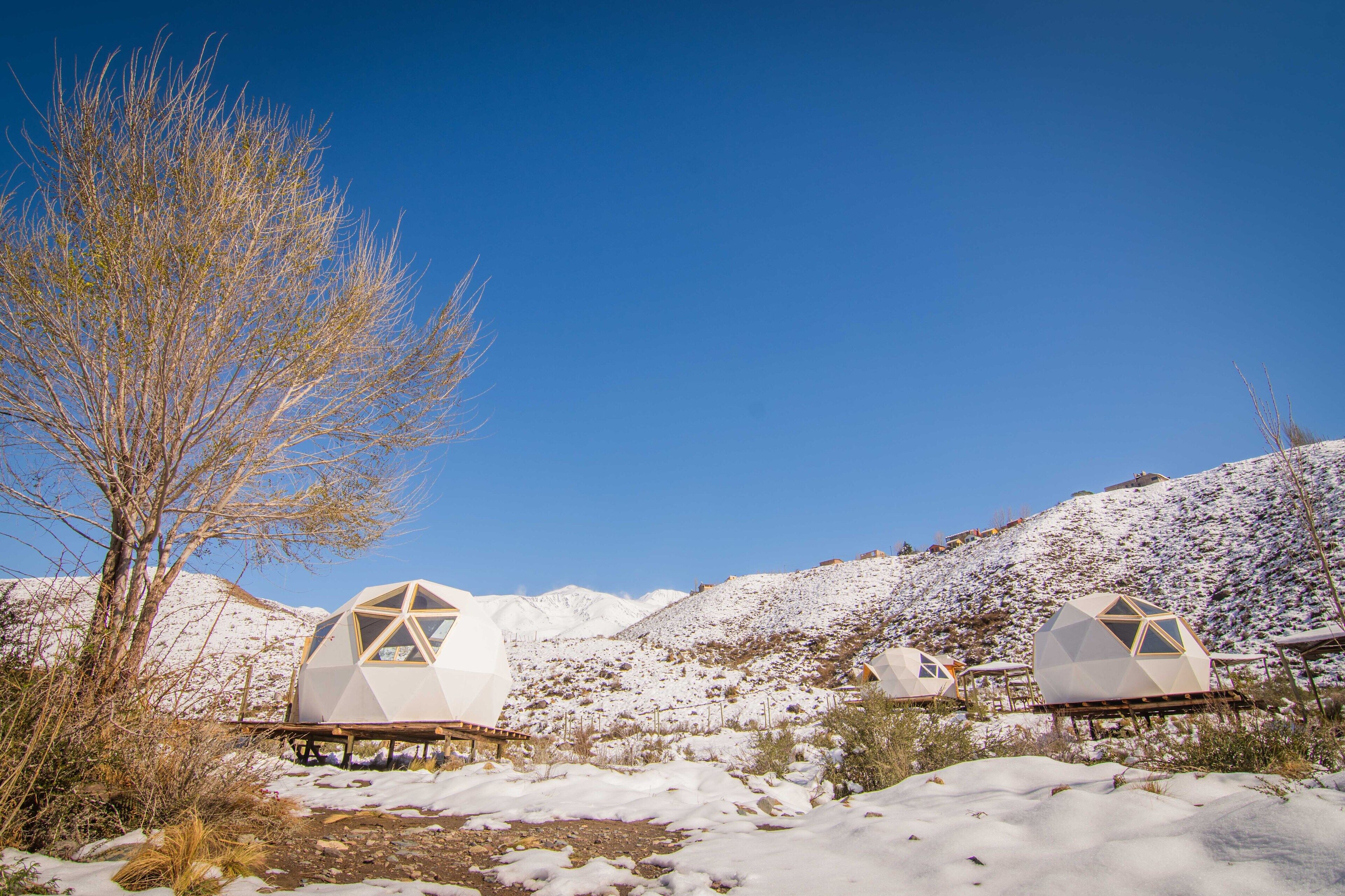 Geodesiska kupolkonstruktioner i ett snötäckt landskap med berg i bakgrunden.