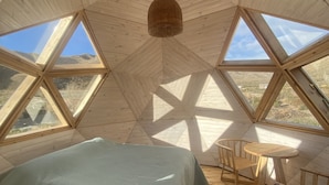 A cozy, triangular room with a bed, a table, and chairs, large windows offering a view of the outdoors. - Domos Andinos HostCamp  (Potrerillos)