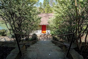 Un escalier menant à un bâtiment doté d’une porte rouge, entouré d’arbres.