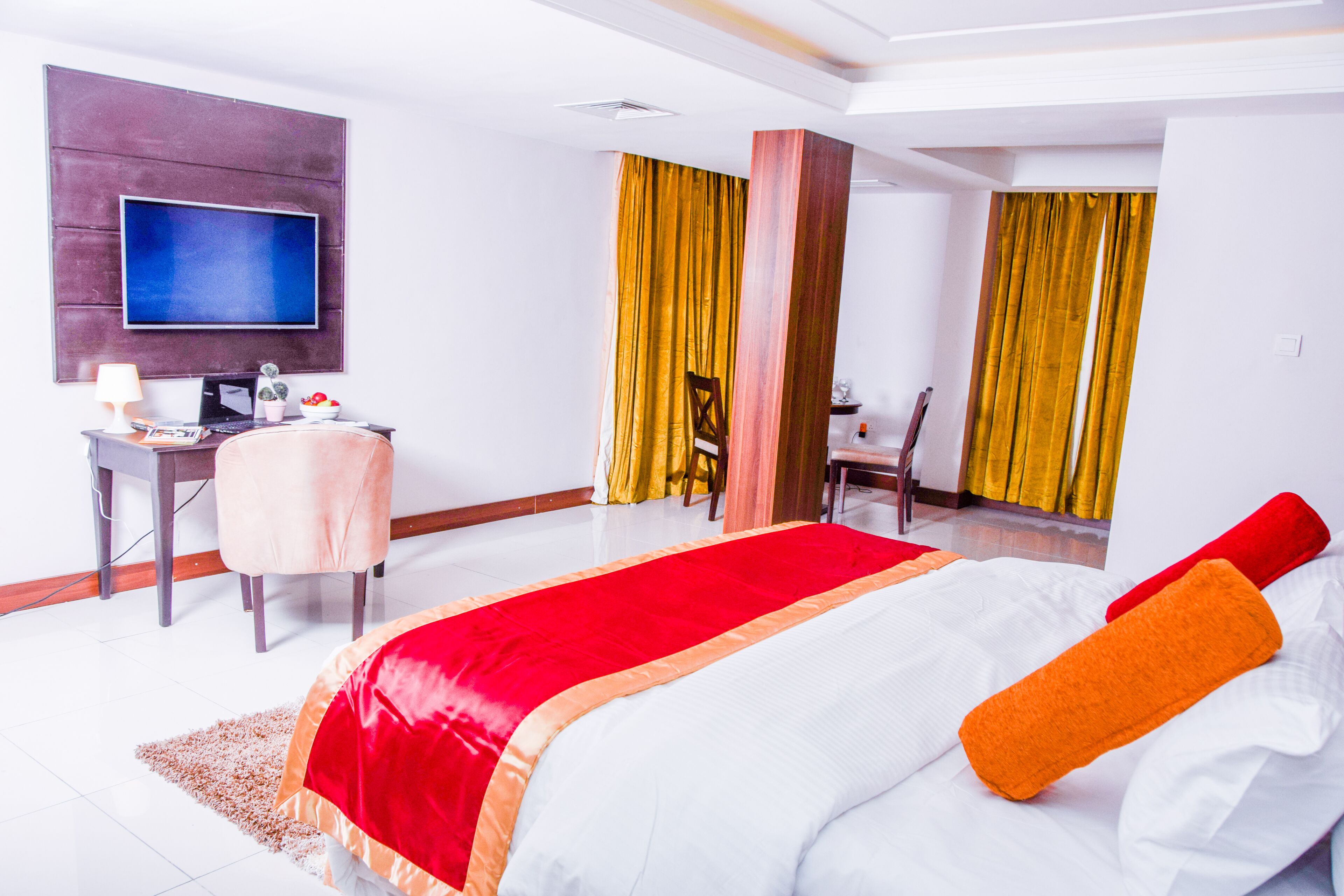 Ein Hotelzimmer mit einem großen Bett, einem Schreibtisch, einem Sessel, einem Fernseher und Vorhängen.