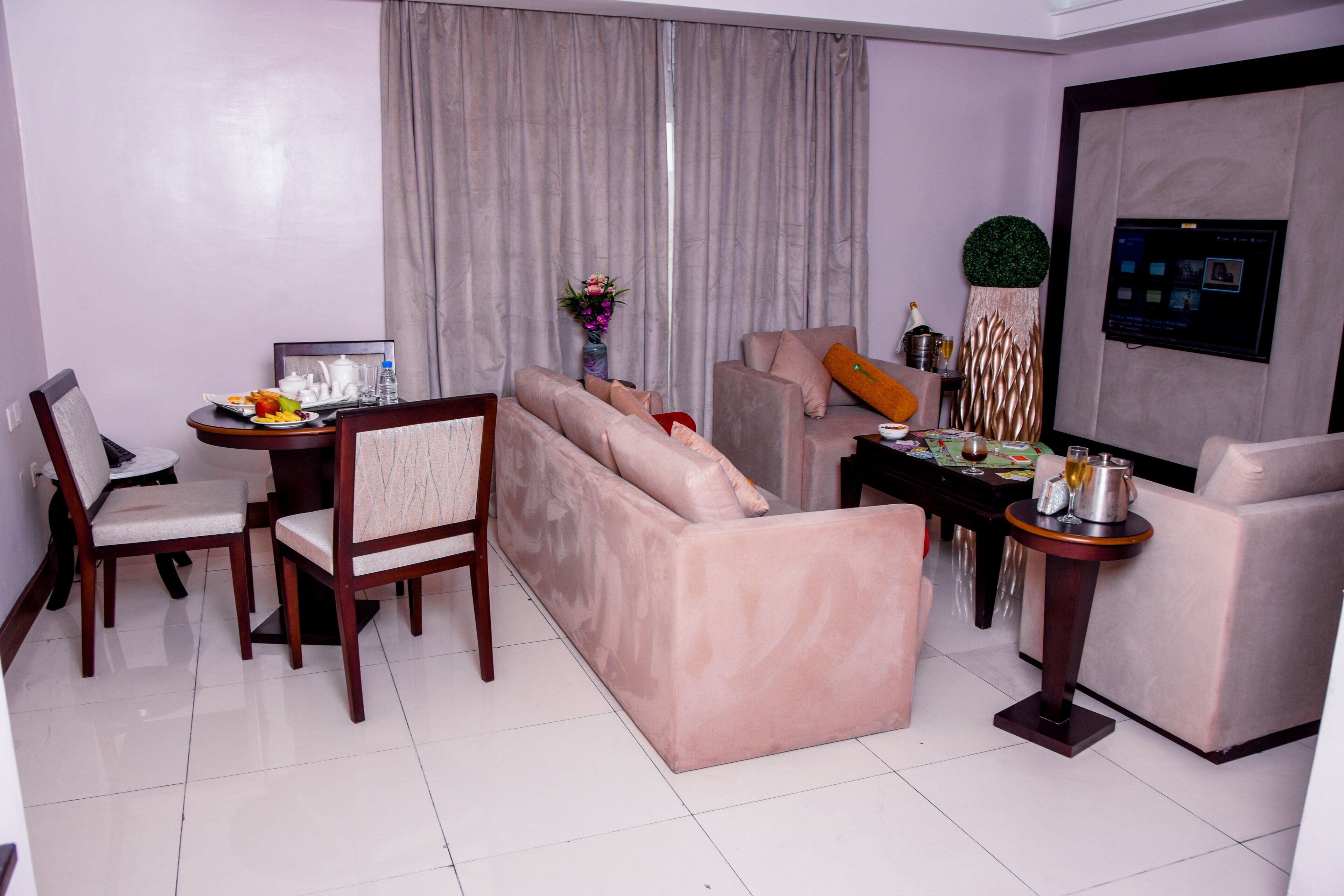 A modern living room with a sofa, chairs, a dining table, and a TV mounted on the wall.