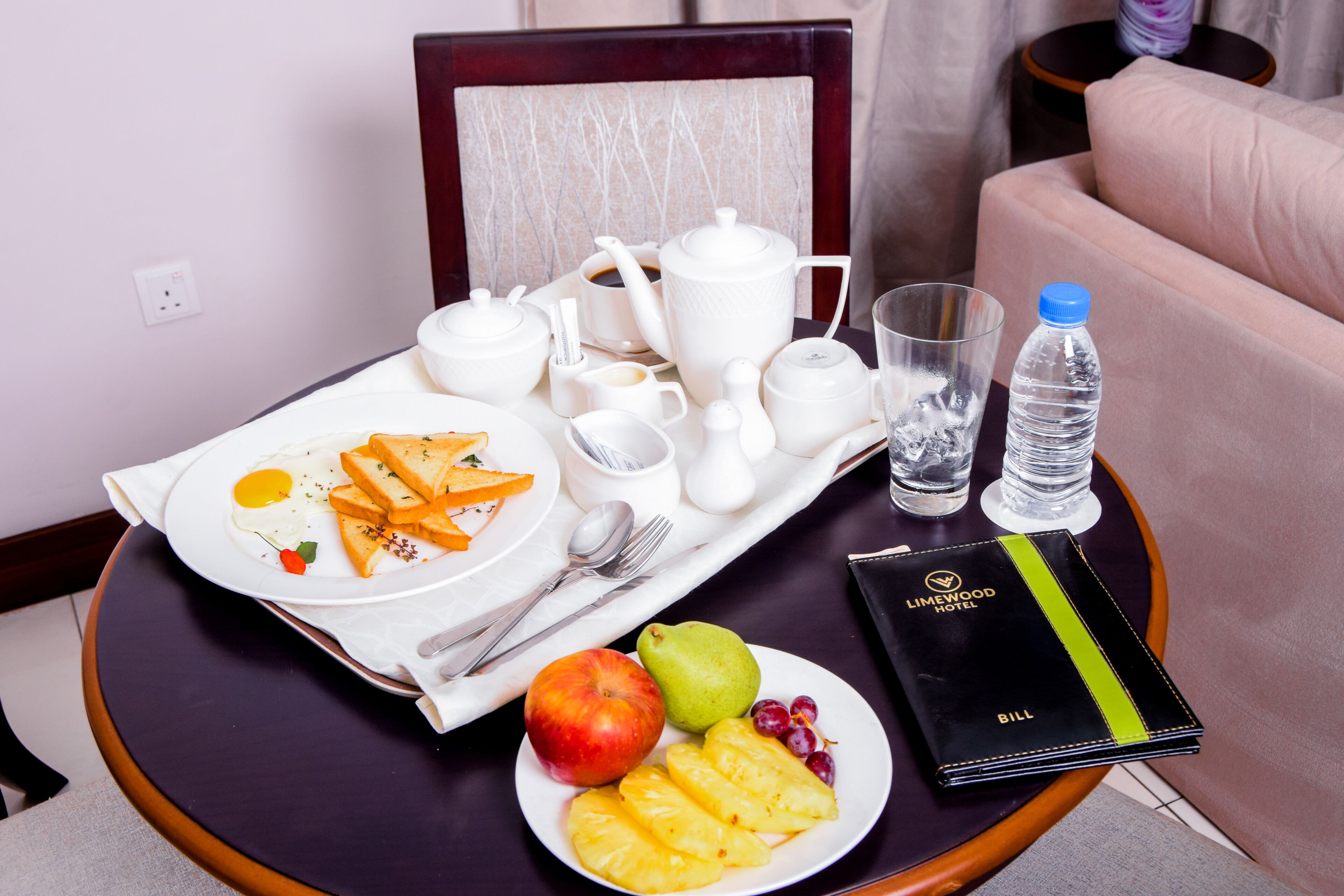 Ein Tablett mit Frühstücksgebäck, Eiern, Obst und einer Wasserflasche auf einem Tisch.