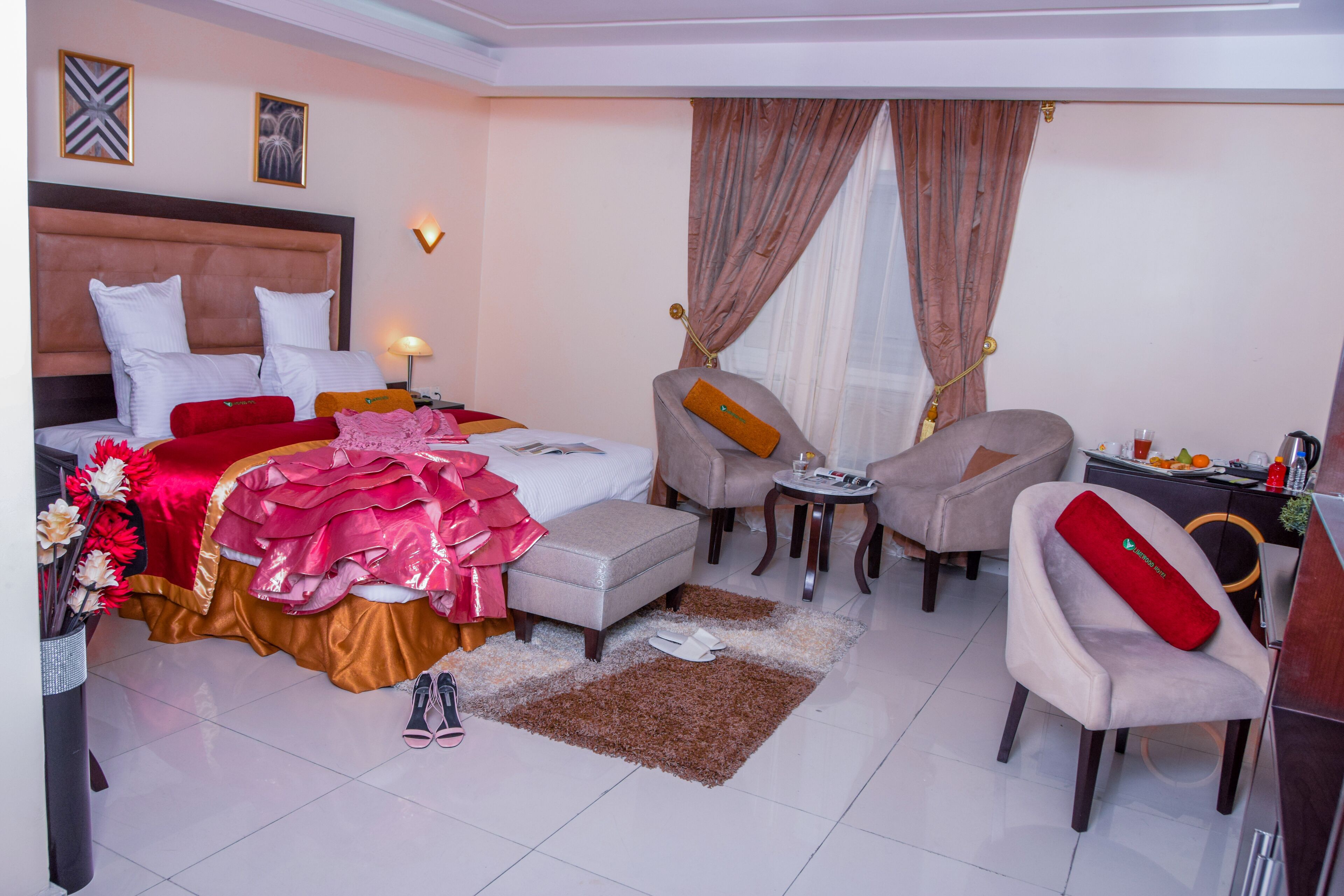 A hotel room with a bed, a sitting area with a table and chairs, a small kitchenette, and a window with curtains.